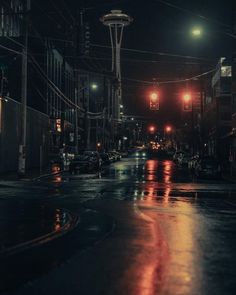 an empty city street at night with traffic lights and buildings in the background on a rainy day