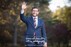 a man in a suit and tie waves to the camera with his hand raised up