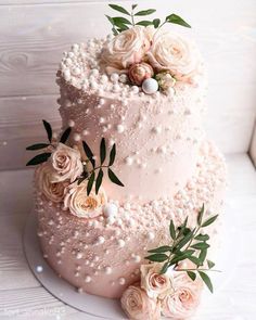 a three tiered wedding cake with pink flowers on top and greenery around the edges