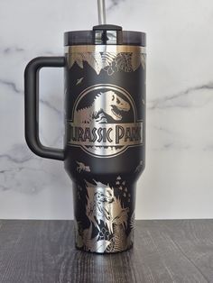 a black and gold travel mug sitting on top of a wooden table next to a marble wall