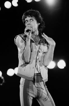 the man is singing on stage with his hands in his pockets and holding a microphone to his mouth