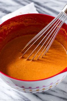 a bowl filled with sauce and whisk on top of a marble countertop