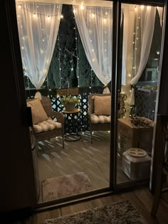 an open patio door with curtains and lights on the outside, looking out onto a deck area