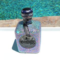 an empty bottle sitting next to a pool filled with blue and green water, covered in holographics