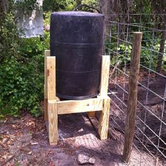 a large black barrel sitting on top of a wooden stand next to a wire fence