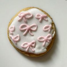 a cookie decorated with pink bows and icing on a white table top, ready to be eaten