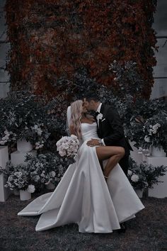 a bride and groom are kissing in front of some flowers on the grass with their arms around each other