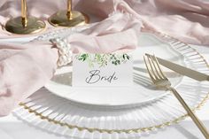 a white plate topped with a place card on top of a pink cloth covered table