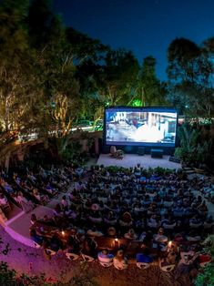 an outdoor movie theater at night with people sitting in the seats and watching something on the screen