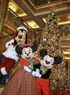 two mickey and minnie mouse characters standing in front of a christmas tree