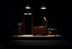 a man standing in front of a desk on top of a stage