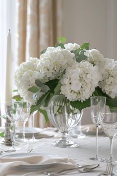 white flowers are in glass vases on a table set with silverware and wine glasses