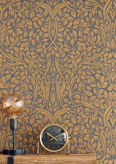 a clock sitting on top of a wooden table next to a wallpapered wall