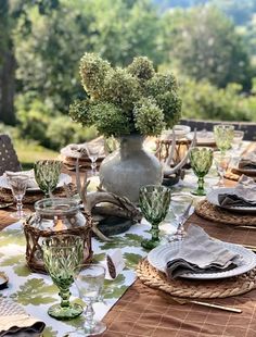 an outdoor table set with place settings and flowers in a vase on the centerpiece