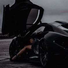 a woman sitting in the open door of a black sports car