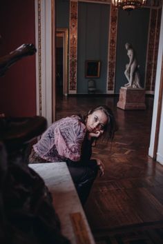 a woman is sitting on the floor in a room with statues and chandeliers