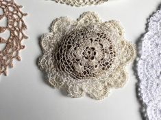 three crocheted doily are laying on a white tablecloth, one is brown and the other is beige