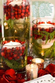 some candles are sitting on a table with red flowers and greenery in glass vases