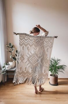 a woman standing in front of a macrame wall hanging on a wooden floor