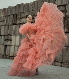 a woman in a long pink dress standing next to a stone wall