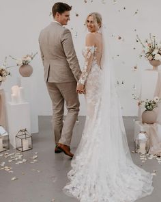 a bride and groom holding hands in front of a backdrop with flowers on the floor