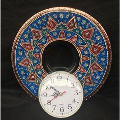 a clock sitting on top of a blue and red plate with an intricate design around it