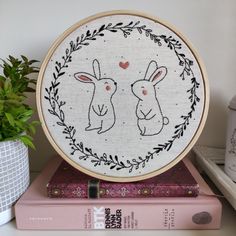 two rabbits in a frame on top of some books and a potted plant next to it