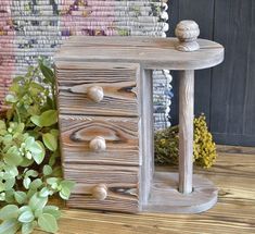 a small wooden table with drawers and knobs on the top, next to some plants