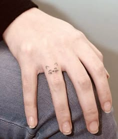 a woman's hand with a cat tattoo on her left thumb and the other half of her finger