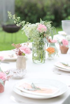 the table is set with flowers in vases, plates and napkins on it