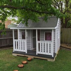 a small gray and white shed sitting on top of a lush green field next to a tree