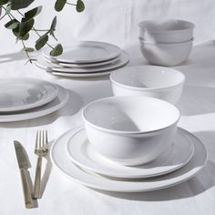 white dishes and silverware are arranged on a tablecloth with eucalyptus branches in the background