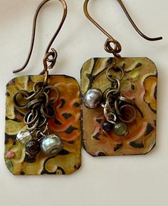 Created over morning coffee in our "studio," two sisters-turned-nextdoor-neighbors have crafted this one of a kind pair of earrings. The earrings are handmade of recycled tin, upcycled chain bits from a thrifted necklace and copper findings.  Back piece is made from a recycled tin that has been primed, cut, embossed, painted or collaged, distressed, darkened, then top coated for protection. On top of that is a bit of chain and beads as a dangle.  These are truly unique, handmade and artisan. Our earrings are ultra light weight due to being made of paper and tin. Don't be mistaken, though; they are durable and protected and will stand up to normal wear and tear.  Last of the photos shows the back of the earring. see video for size reference. these are on the smaller side. Recycled Tin, Artisan Earrings, Back Pieces, Emboss, Jewelry Earrings Dangle, Dangle Drop Earrings, Dangle Earrings, Jewelry Earrings, Drop Earrings