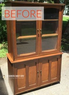 an old china cabinet with glass doors on the top and bottom, sitting in front of a tree