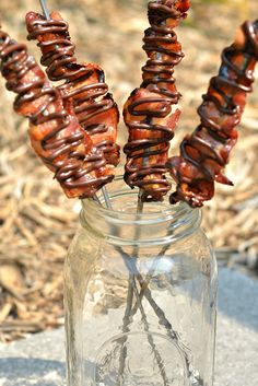 several skewers of food sitting in a mason jar on the ground next to dry grass