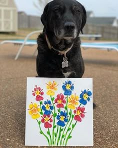 a black dog is holding a card with flowers on it