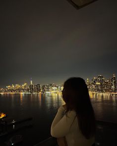 a woman is looking out over the water at night with city lights in the background