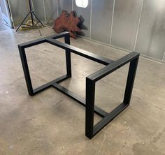 two black metal tables sitting on top of a cement floor in front of a wall