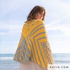 a woman is standing on the beach wearing a yellow and gray crocheted shawl