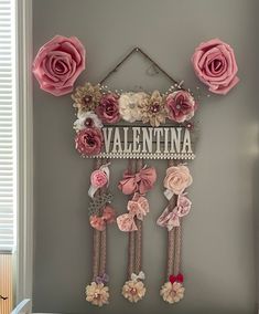 a pink and white wall hanging with paper flowers on it's side in front of a window