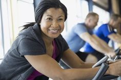 a woman is smiling as she rides an exercise bike with other people in the background