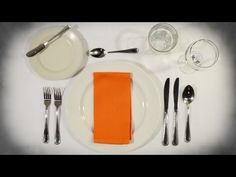 a white plate topped with silverware and an orange napkin next to utensils