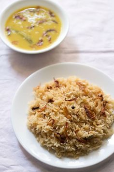 a white plate topped with rice next to a bowl of soup and a silver spoon