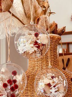 three glass ornaments hanging from a wicker basket filled with dried flowers and leaves in them