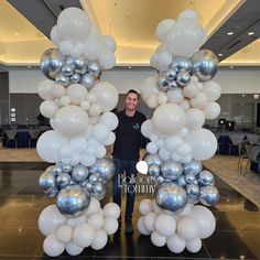 a man standing in front of a giant balloon arch with silver and white balloons on it