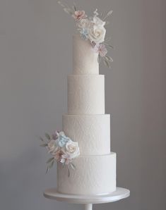 a three tiered white wedding cake with pink and blue flowers on the top layer