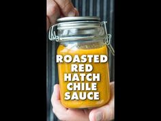 a person holding a jar with mustard in it that says roasted red hatch chile sauce