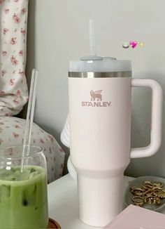 a pink coffee cup sitting on top of a table next to a green smoothie