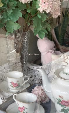 pink flowers are in a vase next to tea cups and saucers