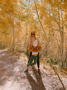 a woman standing in the middle of an autumn forest